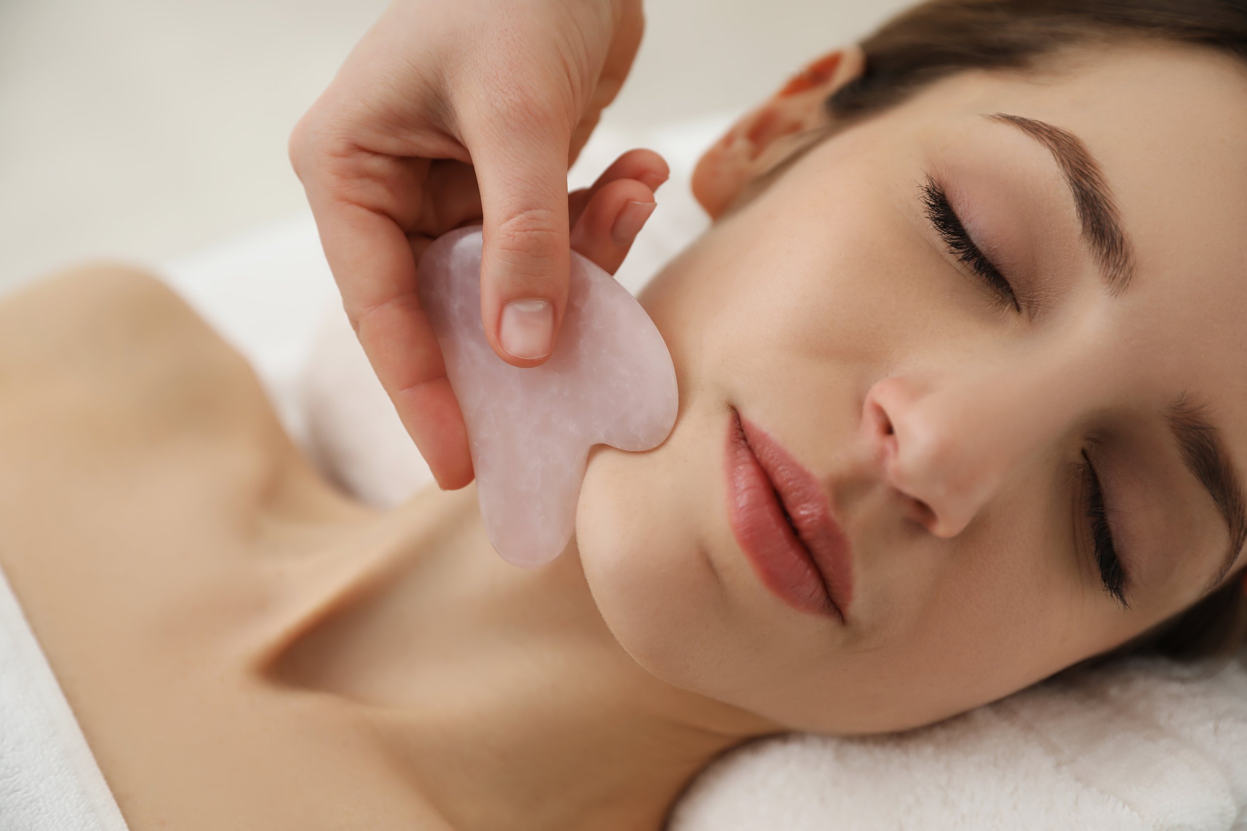 Young,Woman,Receiving,Facial,Massage,With,Gua,Sha,Tool,In